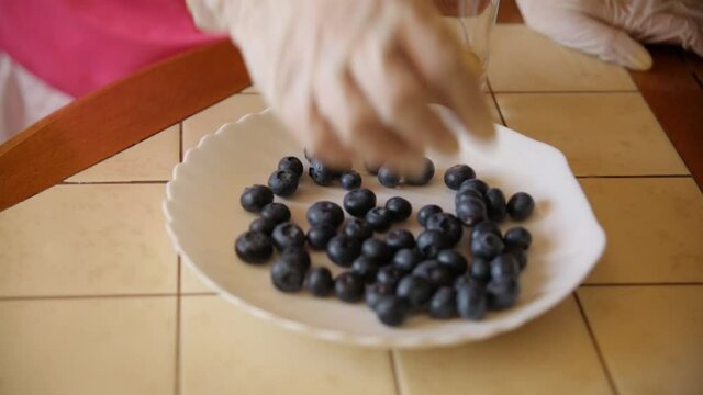 A female hand collects blueberries from a plate into a glass.