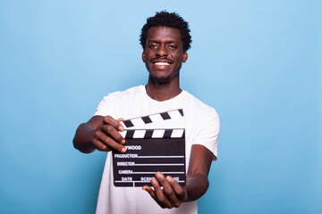 Portrait of man holding clapperboard to cut scenes in movie making industry. Casual person showing board to camera and smiling while having filmmaker object for cinematography - obrazy, fototapety, plakaty