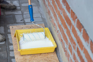 Yellow paint tray with primer and wolf. Impregnation of walls in open air