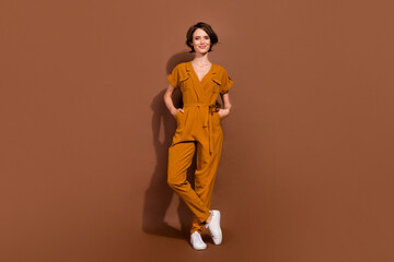 Fototapeta premium Full size photo of attractive charming young woman hands pockets smile lady isolated on brown color background