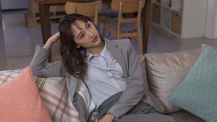 asian lady in grey business suit resting at home thinking with unpleasant look. trouble at work...