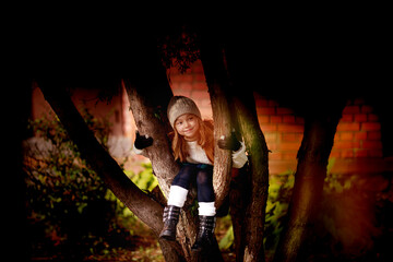 Obraz premium dressed in autumn clothes cute girl sitting on a tree