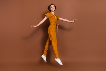 Fototapeta na wymiar Full length photo of happy nice cheerful young woman jump go empty space isolated on brown color background