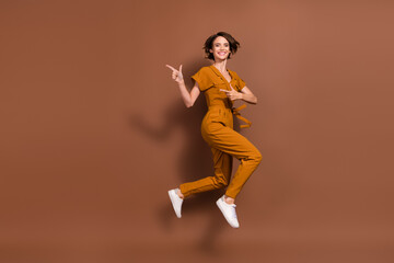 Fototapeta na wymiar Full size photo of happy nice young woman jump point fingers empty space isolated on brown color background