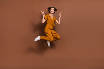 Fototapeta na wymiar Full body photo of positive joyful happy young woman jump make finger v-sign isolated on brown color background