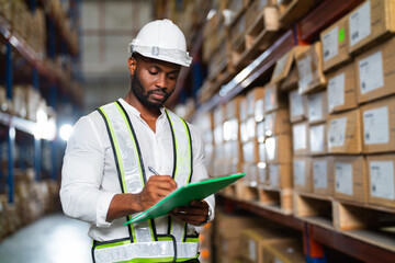 Portrait of an African warehouse manager holding a clipboard checking inventory in a large...