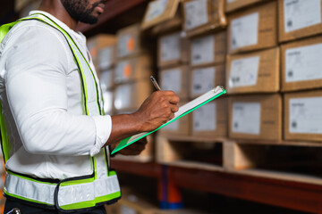Portrait of an African warehouse manager holding a clipboard checking inventory in a large...