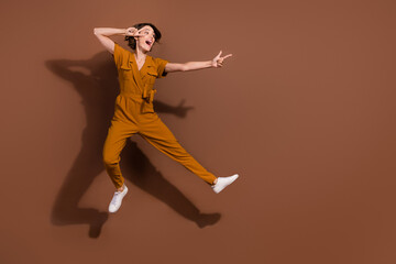 Full size photo of positive nice happy young woman jump look point empty space isolated on brown color background