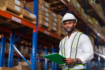 Portrait of an African warehouse manager holding a clipboard checking inventory in a large distribution center.