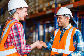 Two warehouse workers shaking hand when success project or first time greeting in a distribution center warehouse.
