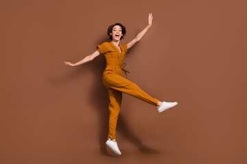 Fototapeta na wymiar Full body photo of cheerful excited happy young woman jump up raise hands isolated on brown color background
