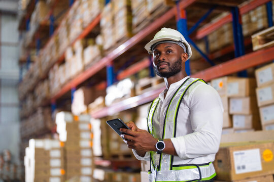 Warehouse worker working process checking the package with a tablet in a large distribution center. an African male supervisor inspects cargo delivery status.