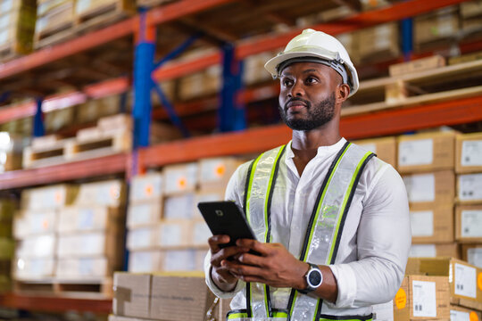 Warehouse worker working process checking the package with a tablet in a large distribution center. an African male supervisor inspects cargo delivery status.