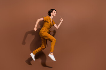 Fototapeta na wymiar Full body photo of happy joyful young woman jump up run empty space sale news isolated on brown color background