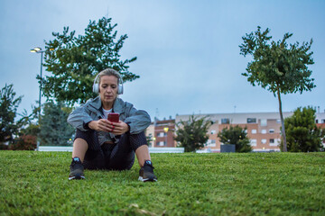 Sporty Woman Using Phone.
Blonde Woman Resting After Doing Her Daily Exercise Routine. She Is Using Her Mobile Phone To Listen To Music With Headphones.
