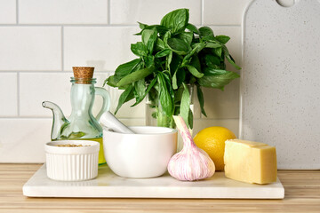 Italian pesto sauce ingridients for cooking. Fresh basil leaves, hard parmesan cheese, garlic, olive oil in bottle, pine nuts, lemon. Grind and mortar. Mediterranean recipe. Homemade national cuisine