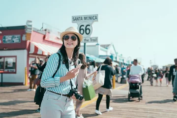 Fototapete Route 66 end of route 66 on santa monica pier california. happy smiling young asian chinese woman backpacker holding smartphone and camera joyful looking aside under sunshine. pretty tourist enjoy sun flare  © PR Image Factory