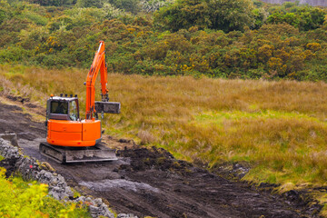 Small orange color mini digger working in a field with a wide bucket. Heavy machinery equipment....