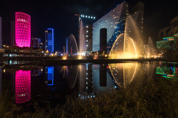 Singing light and music fountain on background of panorama of beautiful buildings at night.