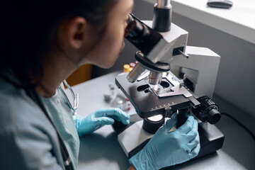 Young worker works with microscope researching material at table in laboratory