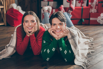 Photo portrait young couple wearing ugly sweaters laying on floor on xmas holidays under plaid blanket