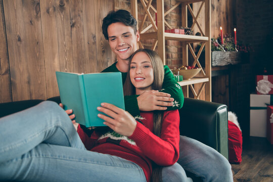 Photo portrait cheerful couple smiling spending winter holidays together reading book embracing on couch