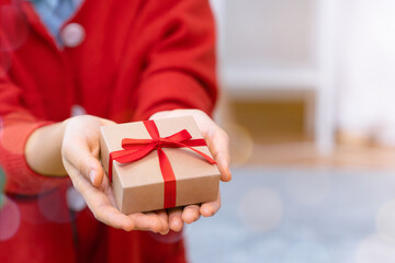 Close-up woman hands holding craft gift box with red ribbon.
