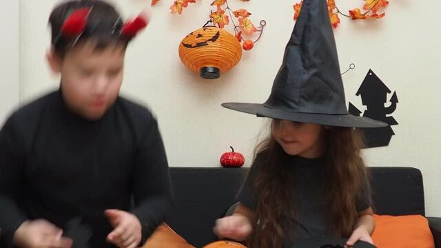 boy and girl celebrate halloween at home. eat sweets and gummy worms. girl in a witch hat and a boy with devil horns. having fun at home. family, happiness, holidays