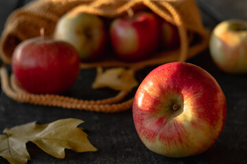 A fresh red apple close-up near a yellow knitted bag on a wooden table in an apple orchard.