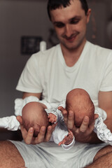Father holding newborn twins on his arms. Close-up portrait of heads of newborn twins. Young father looking with love to his newborn daughters. Selective focus. Film grain