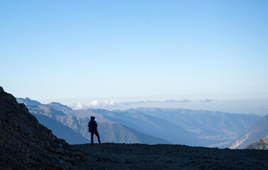 The silhouette of a man against the backdrop of mountains and clouds.