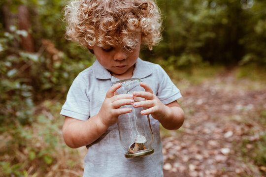 Cute boy holding glass jar with snails in forest