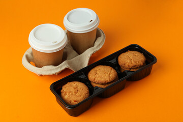 Cookies and paper cups of coffee on orange background