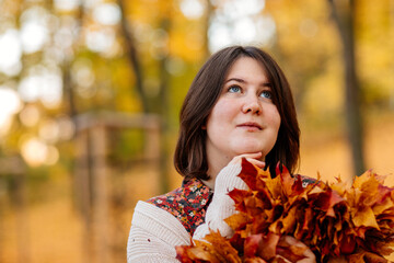 Portrait of beautiful romantic young woman with autumn yellow brown and red leaves, Close-up of a cute stylish girl in park holding golden leaves, Selective focus, natural light shot, vibrant colors