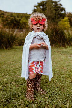 Cute blond boy wearing cape and boots standing on meadow