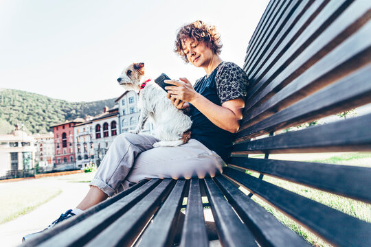 Mid adult woman sitting with pet dog while using smart phone on bench