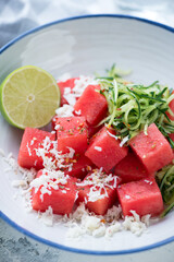 Close-up of summer salad with watermelon cubes, grated bryndza cheese and cucumber served in a white plate, vertical shot