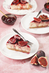 A piece of cake on a white plate on a pink surface: no bake cheesecake with dark red jelly and fig slices