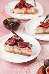 A piece of cake on a white plate on a pink surface: no bake cheesecake with dark red jelly and fig slices