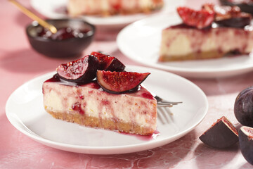 A piece of cake on a white plate on a pink surface: no bake cheesecake with dark red jelly and fig slices
