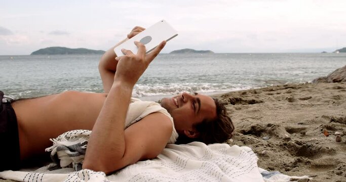 caucasian man lying on beach reading book