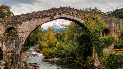 Fototapeta na wymiar Old roman bridge in Cangas de Onis, Asturias, surrounded by a beautiful mountain landscape