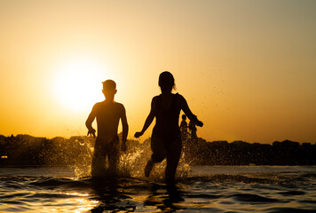Happy kids running and splashing in the sea at sunset. Summer vacation and healthy lifestyle concept