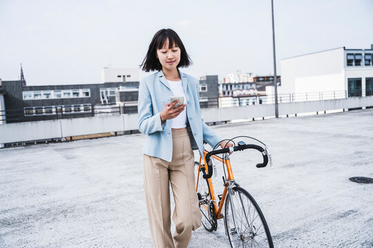Teenage girl with bicycle using mobile phone on rooftop - Powered by Adobe