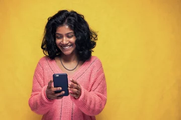 Foto op Aluminium Beautiful Sri Lanka girl makes technology poses with yellow bright background - Young woman uses mobile phone to chatting and messaging © Diego Zarulli