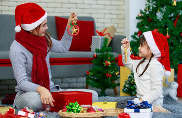 Attractive Asian mother and daughter wearing winter outfits and Santa's hat unboxing gifts celebrating Christmas with joy. Decorated Christmas tree background. Concept for family Christmas party