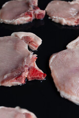 Raw pork chops on black baking tray seasoned with oil and ready for barbecue