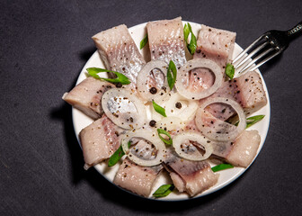 Fillet of salted herring with spices and onions on a plate. Salted sliced ​​fish on a dark...