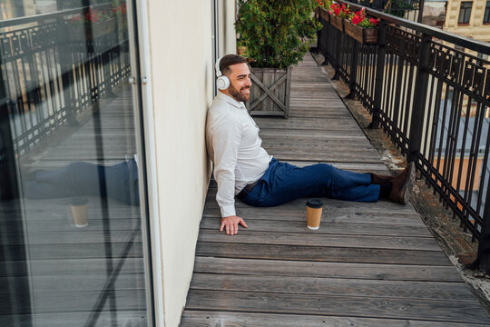 Male professional with reusable cup listening music in office balcony