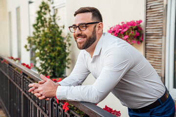 Smiling businessman wearing eyeglasses leaning on railing in office balcony